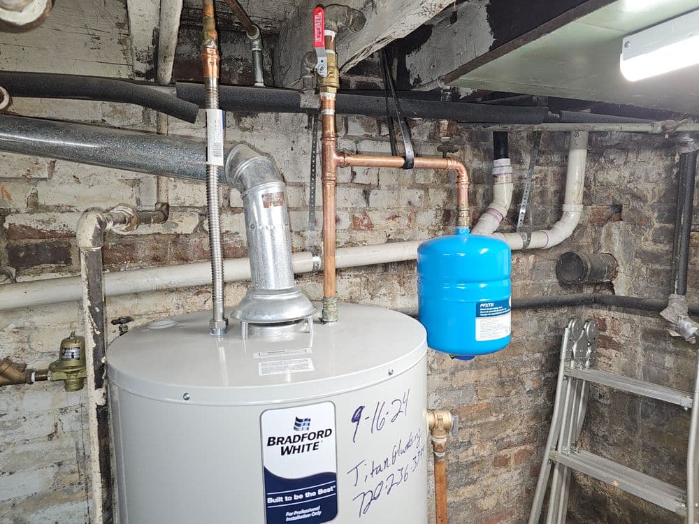 Bradford White water heater with copper pipes and expansion tank in a basement setting.