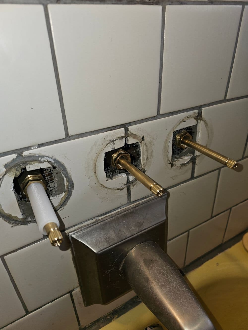 Bathroom faucet installation showing exposed plumbing and valve openings on tiled wall.
